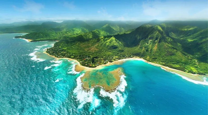 Kauai's north shore reef and bay seen from a helicopter, with green mountain ridges behind