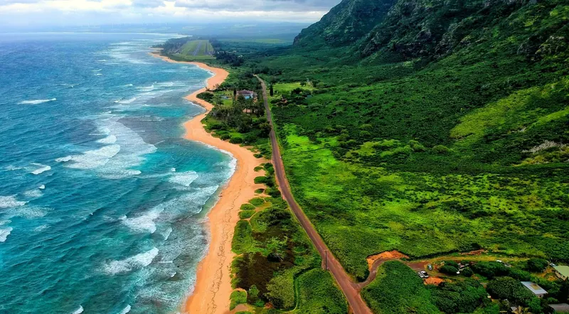 Oahu's north shore from above, with surf breaking along a long sand beach beside green ridges